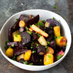 A bowl of roasted beets and carrots garnished with fresh parsley.