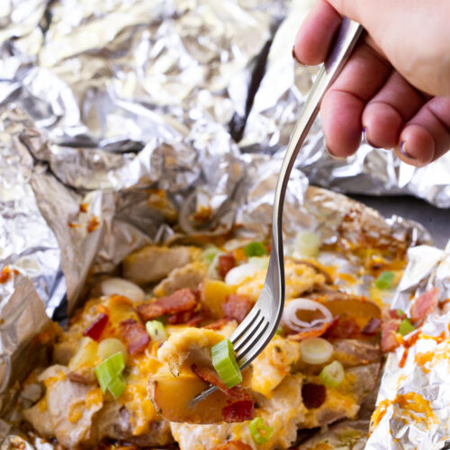 Chicken and potato foil packs topped with cheese, bacon, and green onion.